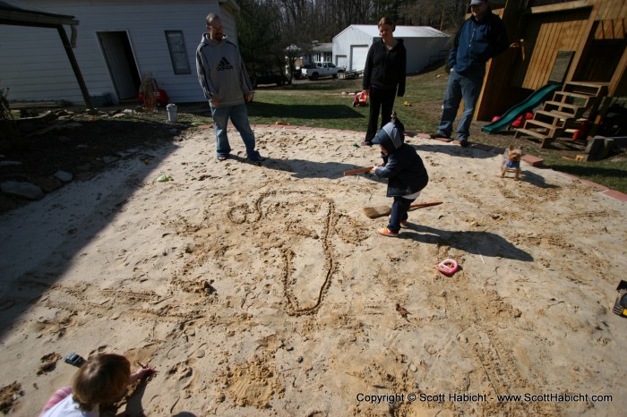 Aspiring artist, Taylor, draws a face in the sand.